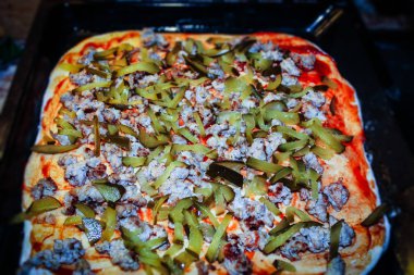 On a black baking sheet, a close-up image shows a pizza made from fresh products: dough, ketchup, pickles, minced meat, boiled egg, onions