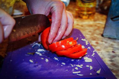 Mutfak masasında bir kadın taze domatesleri pizza bıçağıyla doğruyor.