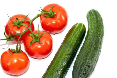 Yeşil dallı taze kırmızı domatesler ve yatay fotoğrafın beyaz arka planında salatalıklar. Tam sebze, suyla yıkanmış, dört domates ve iki salatalık.