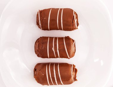 Beyaz bir arka planda beyaz bir tabakta çikolata ve beyaz kremadan yapılmış üç tatlı kek var.