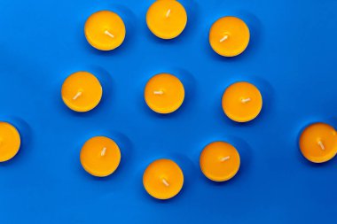 Çember şeklinde 11 tane yanmamış mango kokulu mum mavi bir arkaplanda yatıyor.