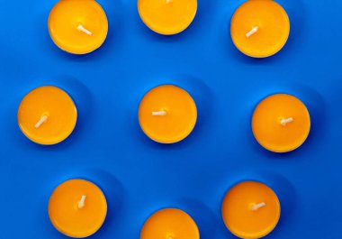 Dokuz tane yanmamış mango kokulu mum daire şeklinde mavi bir arkaplanda yatıyor.