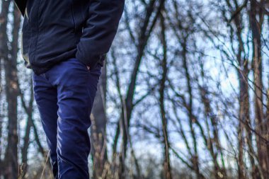 Ceketli ve kot pantolonlu uzun boylu bir adam sokakta duruyor, elleri cebinde..