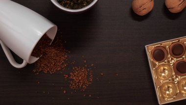 Masanın en üst görüntüsü. Masanın üzerinde bir kutu şeker, iki ceviz, kuru dondurulmuş kahve ile beyaz bir kupa yok. Doğrudan masaya dökülüyor, yapraklı yeşil çay ile zar zor fark edilebilen bir kupa.