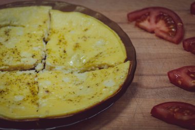 Tabakta taze kahvaltı var. Yumurta ve sütle tereyağlı omlette kızartılmış. Daha uzakta domatesler var, dilimlere bölünmüş.