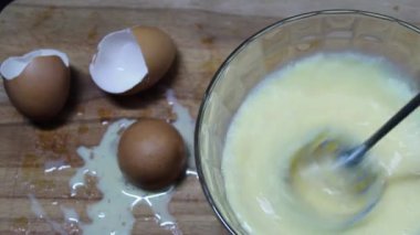 Bir omlet yapma süreci. Bir kasede, çırpıcıyla yumurta ve süt çırp. Arka planda bir yumurta kabuğu var.