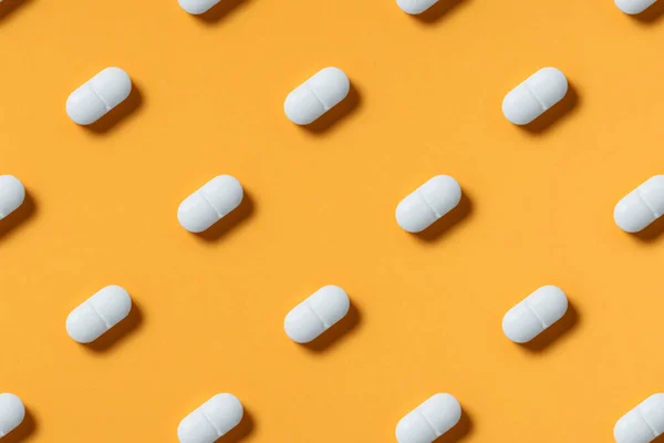 medicine, healthcare and pharmacy concept - white pills or capsules lie in rows diagonal on orange background top view copy space patter
