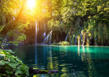 Ünlü Plitvice Gölleri Milli Parkı 'ndaki Idyllic şelalesi yaprakların arasında parıldayan ve güzel çağlayanları su, Lika-Senj ve Hırvatistan' ın manzaralı yansımalarıyla aydınlatan altın güneş ışığı