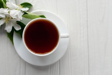 Beyaz porselen fincanda sıcak çay, beyaz çiçekli elma dalı beyaz ahşap arka plan.