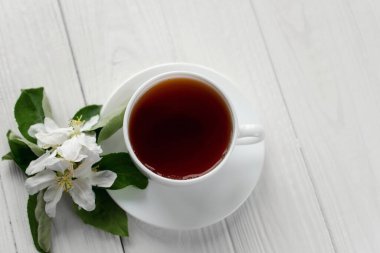 Beyaz porselen fincanda sıcak çay, beyaz çiçekli elma dalı beyaz ahşap arka plan.