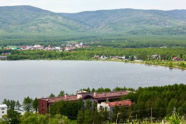 Harika bir panoramik manzara. Görkemli dağların ortasında sisli, temiz bir dağ gölü olan bir göl. Yeşil çimenler. Gölün çevresindeki daireler.