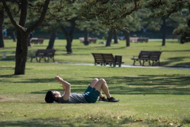 Tokyo / Japonya - 22 Nisan 2018: Kokyogaien Park 'taki çimlerin üzerinde dinlenen adam Tokyo, Japonya' daki İmparatorluk Sarayı 'nın yanında