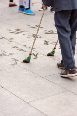 Yaşlı bir adam parkta su kaligrafisi (zemin yazısı - bulaşık) yapıyor. Su kaligrafisi emekli Çinliler arasında popüler bir hobidir.