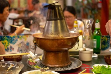 Pekin / Çin - 27 Temmuz 2016: Geleneksel Pekin tarzı Çin kömür ısıtmalı güveç tenceresi, tencerenin etrafında taze malzemeler bulunan bir restoranın yemek masasının ortasına yerleştirildi