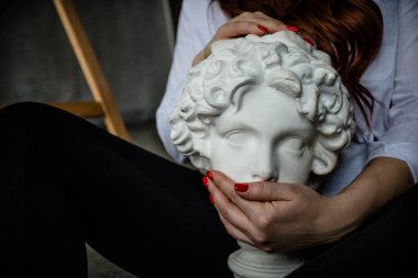 Kahverengi saçlı ve kırmızı manikürlü Avrupalı bir kız alçı büstünün ağzını kapattı.