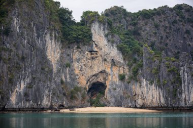 Face-shaped cave with a small beach inside limestone rocks in Lan Ha Bay in Vietnam clipart