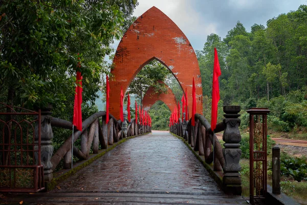 Bridge with archs and red flags in the entrance to My Son Sanctuary in Central Vietnam