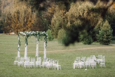 Düğün kemeri dışarıda kumaş ve çiçeklerle süslenmiş. Güzel bir düğün hazırlığı. Bahçedeki yeşil çimlerde düğün töreni. Festival dekorunun bir parçası, çiçek aranjmanı..