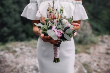 Düğün buketi gelin ellerinde. Genç bir kadın elinde çiçeklerle ayakta duruyor. Kafasız vuruldu.