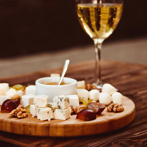 ブドウ、ナッツ類、木製の背景の上に白ワインのグラス添えチーズ ボード — ストック写真