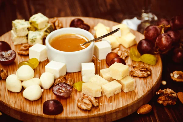 Cheese Board served with grapes, nuts and a glass of white wine on a wooden background — Stock Photo, Image