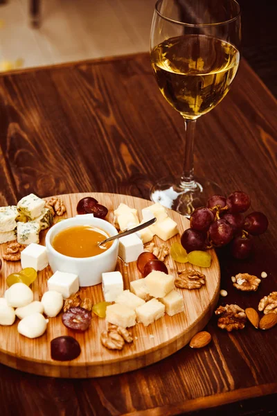 Cheese Board served with grapes, nuts and a glass of white wine on a wooden background — Stock Photo, Image