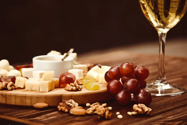 Cheese Board served with grapes, nuts and a glass of white wine on a wooden background — Stock Photo, Image