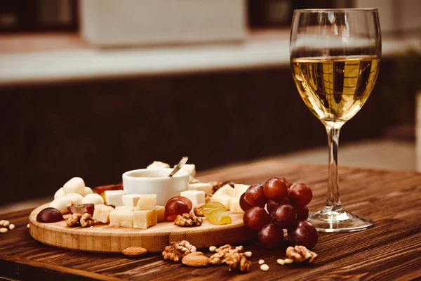 Plateau de fromages servi avec des raisins, des noix et un verre de vin blanc sur fond de bois — Photo