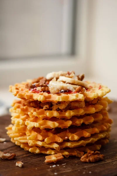 Stack Belgian waffles with walnuts, jam and a banana on a dark wooden background. Sweet food concept.