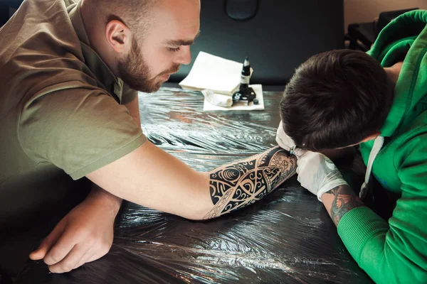 Mester tetováló művész a kesztyű teszi tetoválás a kezét a férfi — Stock Fotó