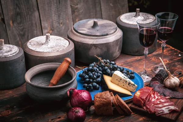 Auswahl an Fleisch- und Käsevorspeisen auf rauem altem Holz mit Trauben, zwei Gläsern Wein und Keramik — Stockfoto