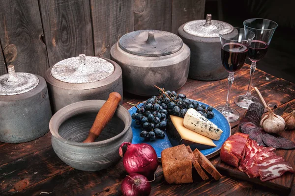 Auswahl an Fleisch- und Käsevorspeisen auf rauem altem Holz mit Trauben, zwei Gläsern Wein und Keramik — Stockfoto