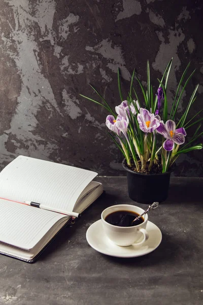 On the table is a Cup of coffee and a vase with flowers crocuses and a blank Notepad — Stock Photo, Image