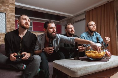 evde bira ve bilgisayar oyunları oynarken elinde joystick ile kanepede oturmuş sakallı erkekler