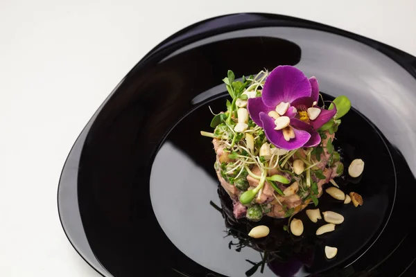 Tártaro saboroso (carne crua) com brotos, amendoins, verdes e flor de orquídea em uma placa preta — Fotografia de Stock