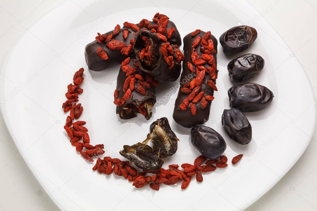 Beautiful sweets with dates and goji berries on white plate