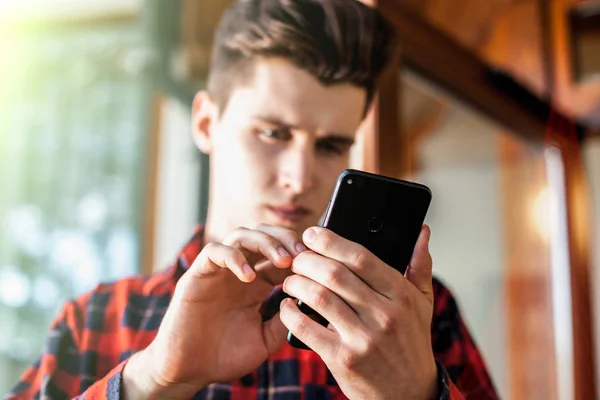 Stílusos jóképű fiatalember egy okos telefon a kezében tartja, és nézett rá — Stock Fotó