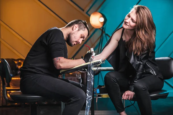 Mestre tatuador faz uma tatuagem na pele da mão cliente menina em uma oficina com equipamento especial — Fotografia de Stock