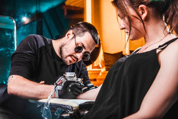 Mistrz tattooist sprawia, że tatuaż na skórze dłoni dziewczyny klienta w warsztacie ze specjalnym wyposażeniem — Zdjęcie stockowe
