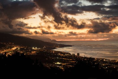 Sahili gösteren manzara ve aydınlanma Puerto de la Cruz şehri İspanya 'nın Tenerife adasında gün batımında bulutlu bir gökyüzü altında