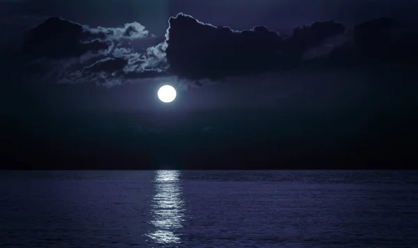 Moon over the sea. Moonlight on the sea. Night sky and swirling beautiful clouds. A patch of moonlight on the surface of the night sea.