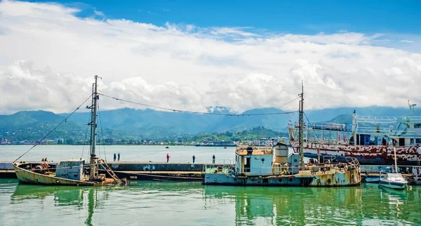 A half-sunken ship at the pier. Sea, mountains and clouds in the background.