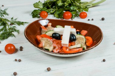 Kahverengi tabakta taze Yunan salatası beyaz desenli masa üzerinde vişneli domates, kırmızı biberli baharatlar ve arka planda yeşil