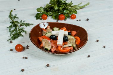 Kahverengi tabakta taze Yunan salatası beyaz desenli masa üzerinde vişneli domates, kırmızı biberli baharatlar ve arka planda yeşil