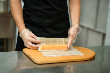 Siyahlı şef geleneksel suşi hazırlıyor. Erkek eli suşi yapıyor. Manzarayı kapat. Metin için boşluk