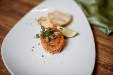 Sarımsaklı somon tartar ve beyaz tabak ahşap masada limon.