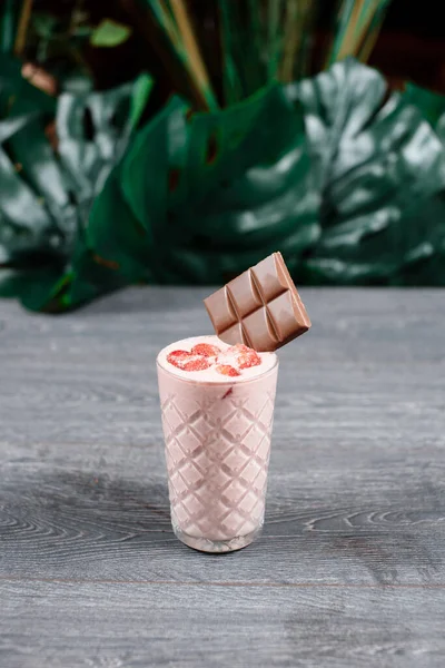 strawberry milkshake with chocolate on grey table with tropical leaves on background. restaurant menu