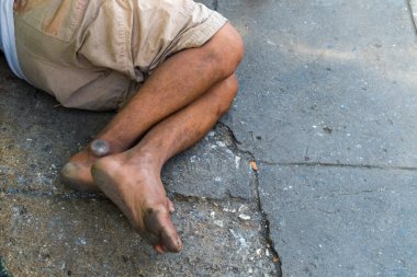 Zavallı evsiz adam ya da mülteci şehrin şehir sokağındaki ahşap bankta bacaklarına odaklanmış uyuyor..