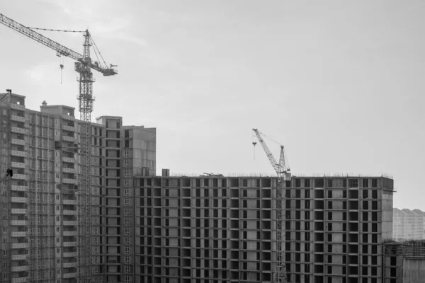 Construction of a large high-rise building with cranes with the grey sky background. Black and White. — Stock Photo, Image