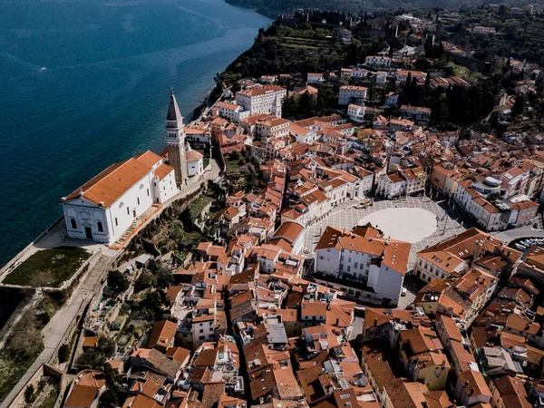 Tartini ana meydanlı Piran kasabası, kırmızı çatılı antik binalar, Slovenya 'nın güneybatısındaki St. George' s Parish Kilisesi ve Adriyatik Denizi üzerinde hava manzarası